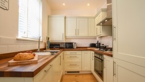 A kitchen with white cabinets, a wooden countertop, a microwave, a stove, and a window with blinds. - The Gallery, Blythburgh (Halesworth)