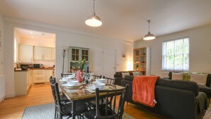 A modern kitchen with white cabinets, a dining table set for four, and a black sofa in the living area. - The Gallery, Blythburgh (Halesworth)