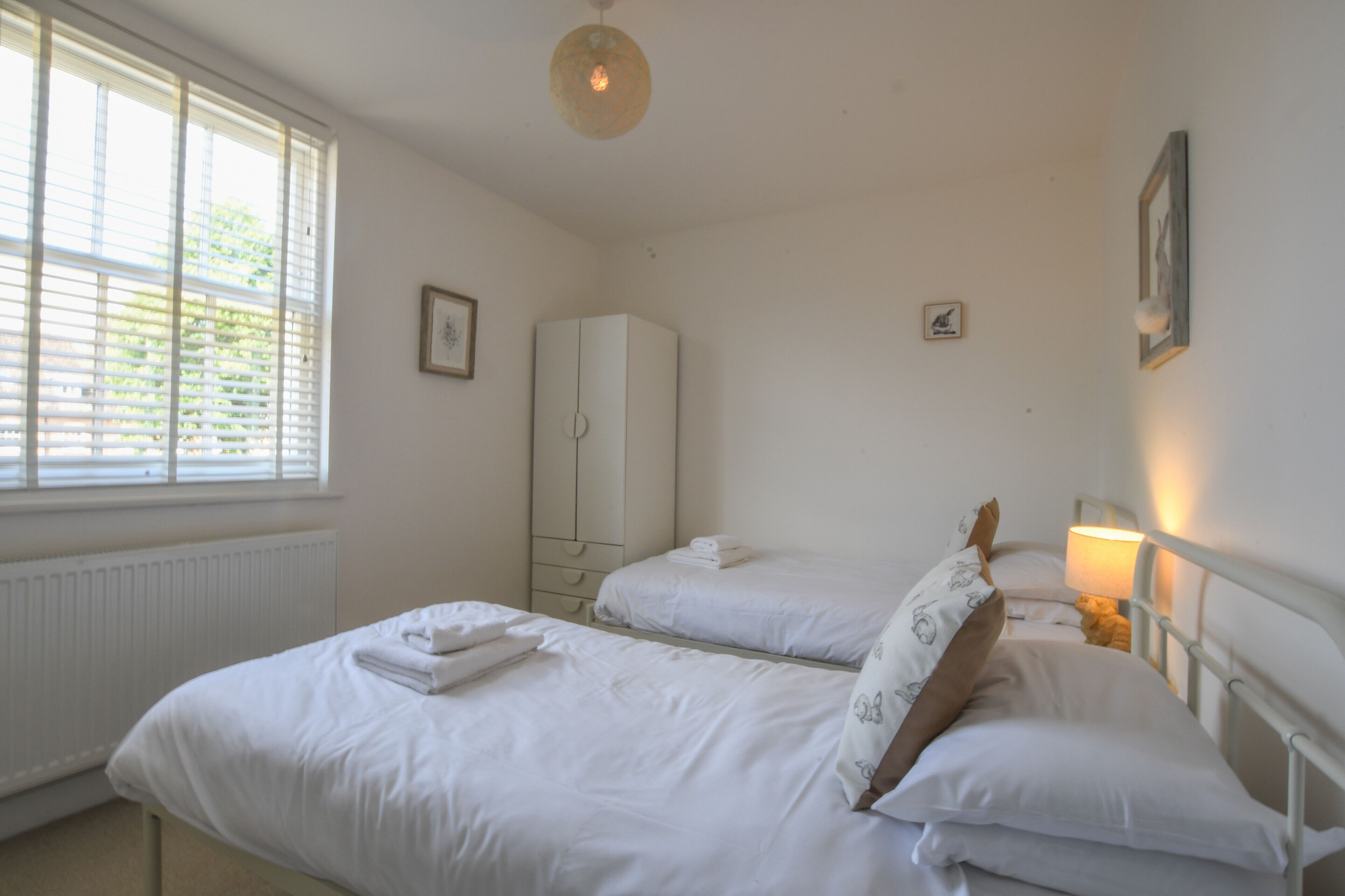 A bedroom with two beds, a wardrobe, and a window with blinds.