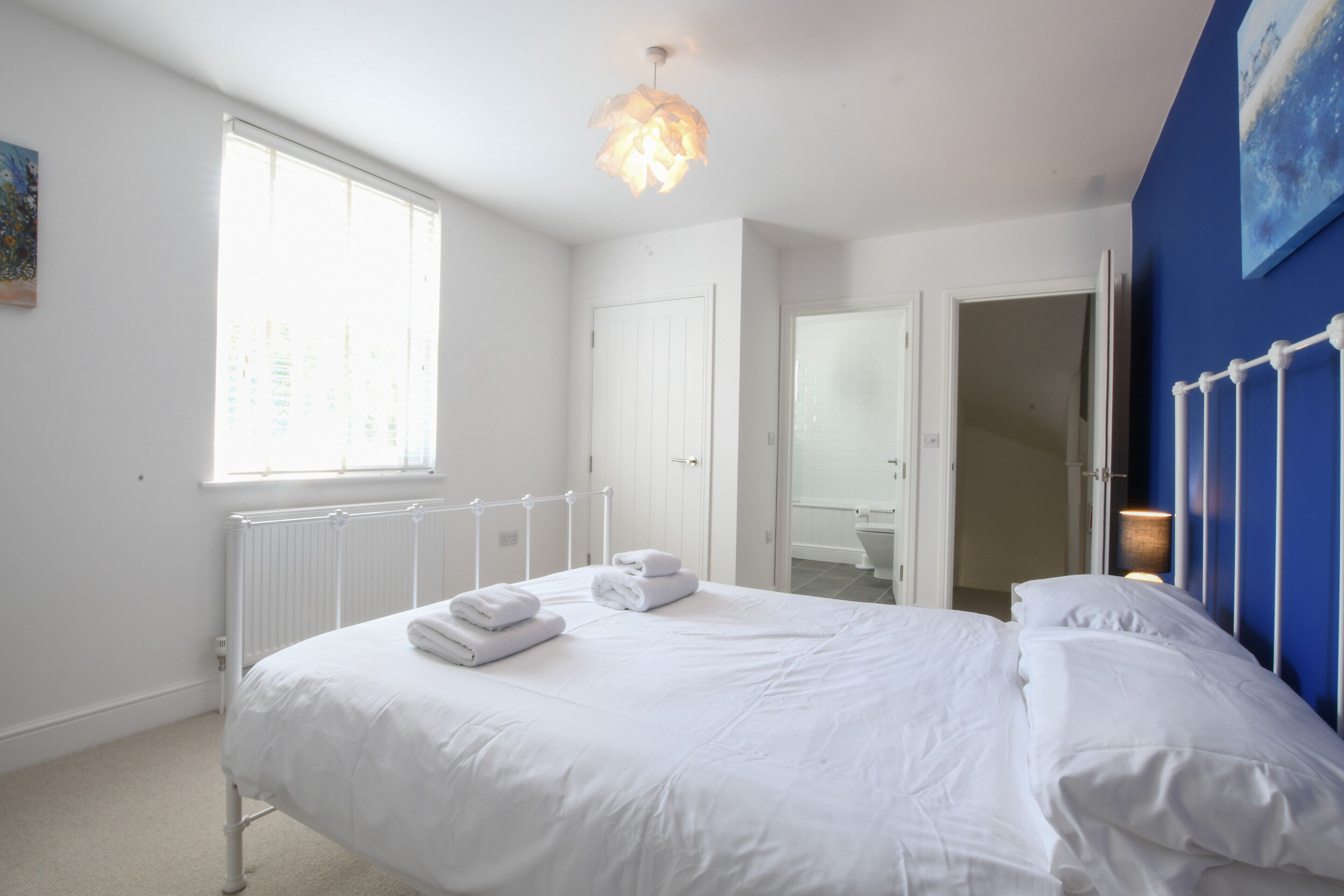 A bedroom with a bed, white bedding, a radiator, a window, and a door leading to a bathroom.