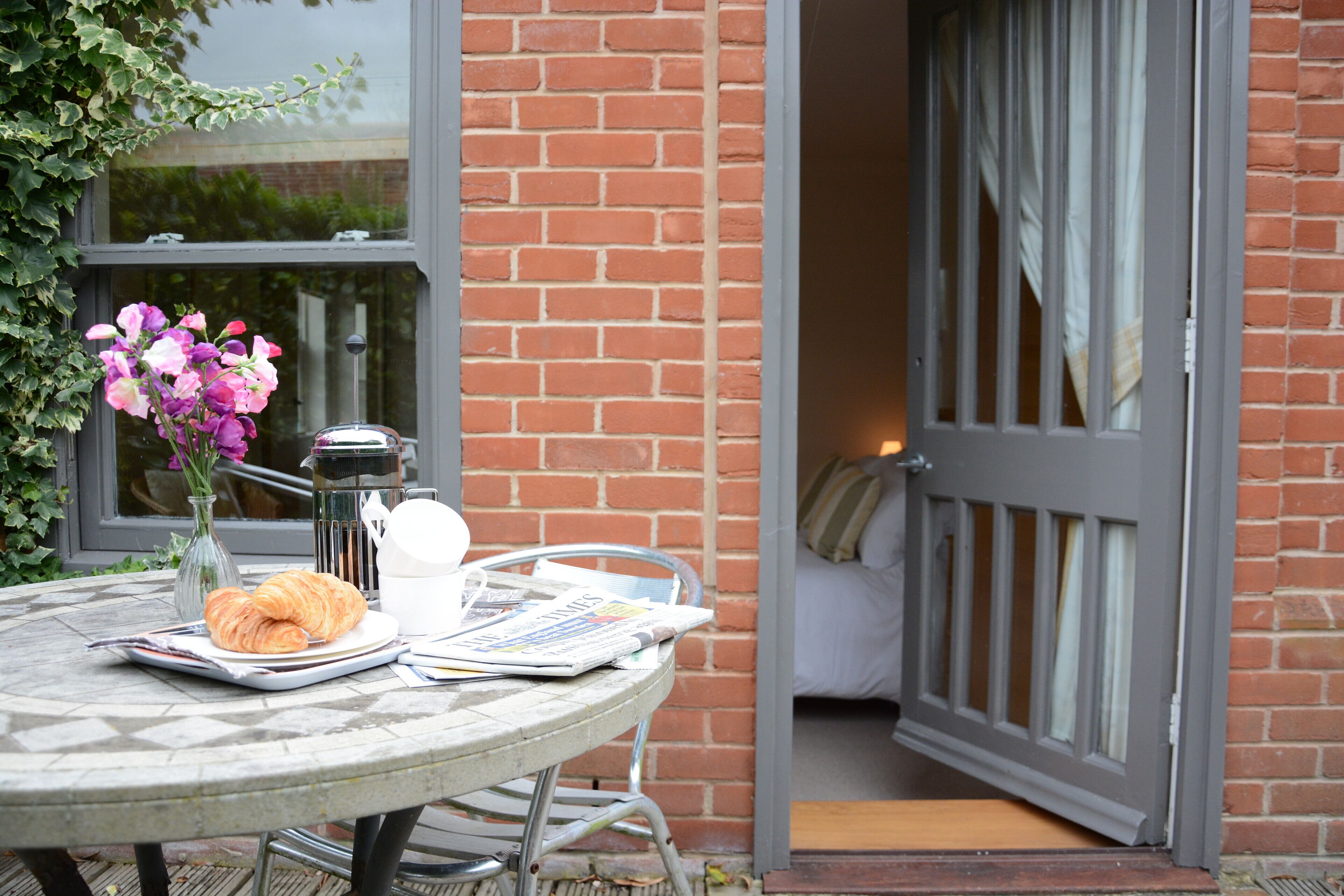 A table with a croissant, a newspaper, and a vase of flowers.