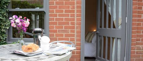 A table with a croissant, a newspaper, and a vase of flowers.