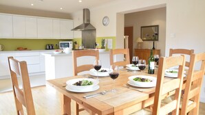 Un coin repas avec une table en bois dressée pour quatre personnes, entourée de chaises en bois. On y trouve des assiettes remplies de nourriture et des verres à vin.