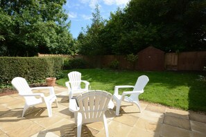 Un espace patio avec quatre chaises en plastique blanches et une petite table, entouré d’un sol carrelé en pierre.