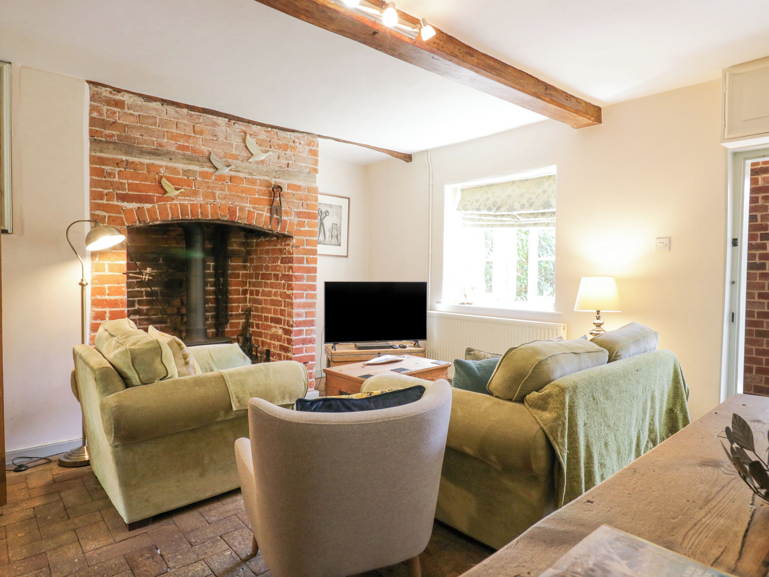 A cozy living room with a brick fireplace, a television, and two green sofas.