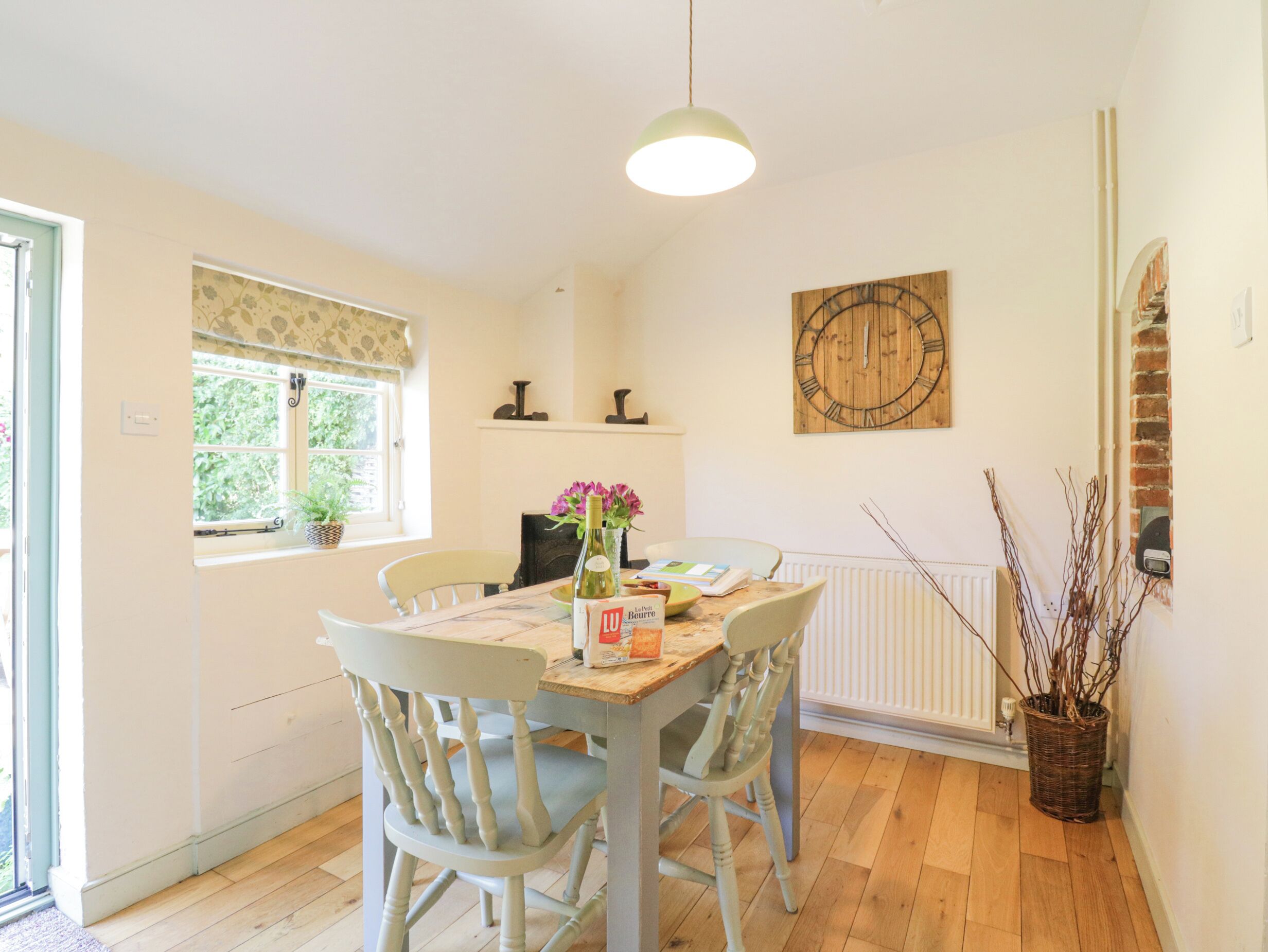 A dining area with a table, chairs, a clock, and a window with a view of greenery.