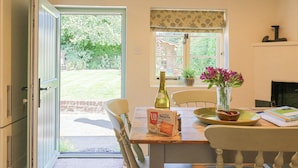 A dining area with a table set for two, a bottle of wine, and a vase of flowers. - Shoemakers Cottage, Friston (Saxmundham)