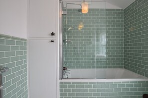 A bathroom with a glass-enclosed shower, green-tiled walls, and a white bathtub. - Driftwood, Southwold (Reydon)