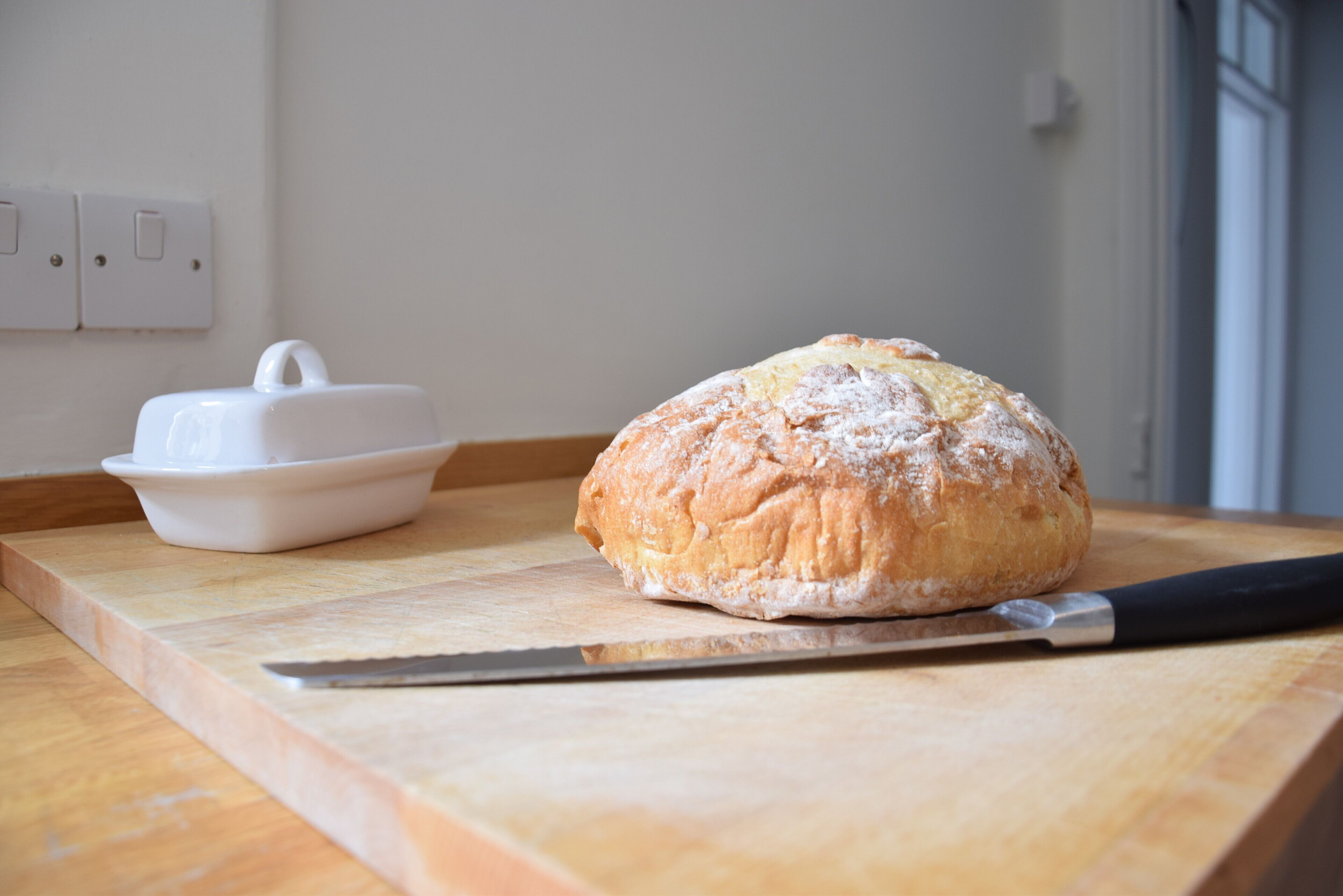 A loaf of bread on a wooden cutting board with a knife beside it.