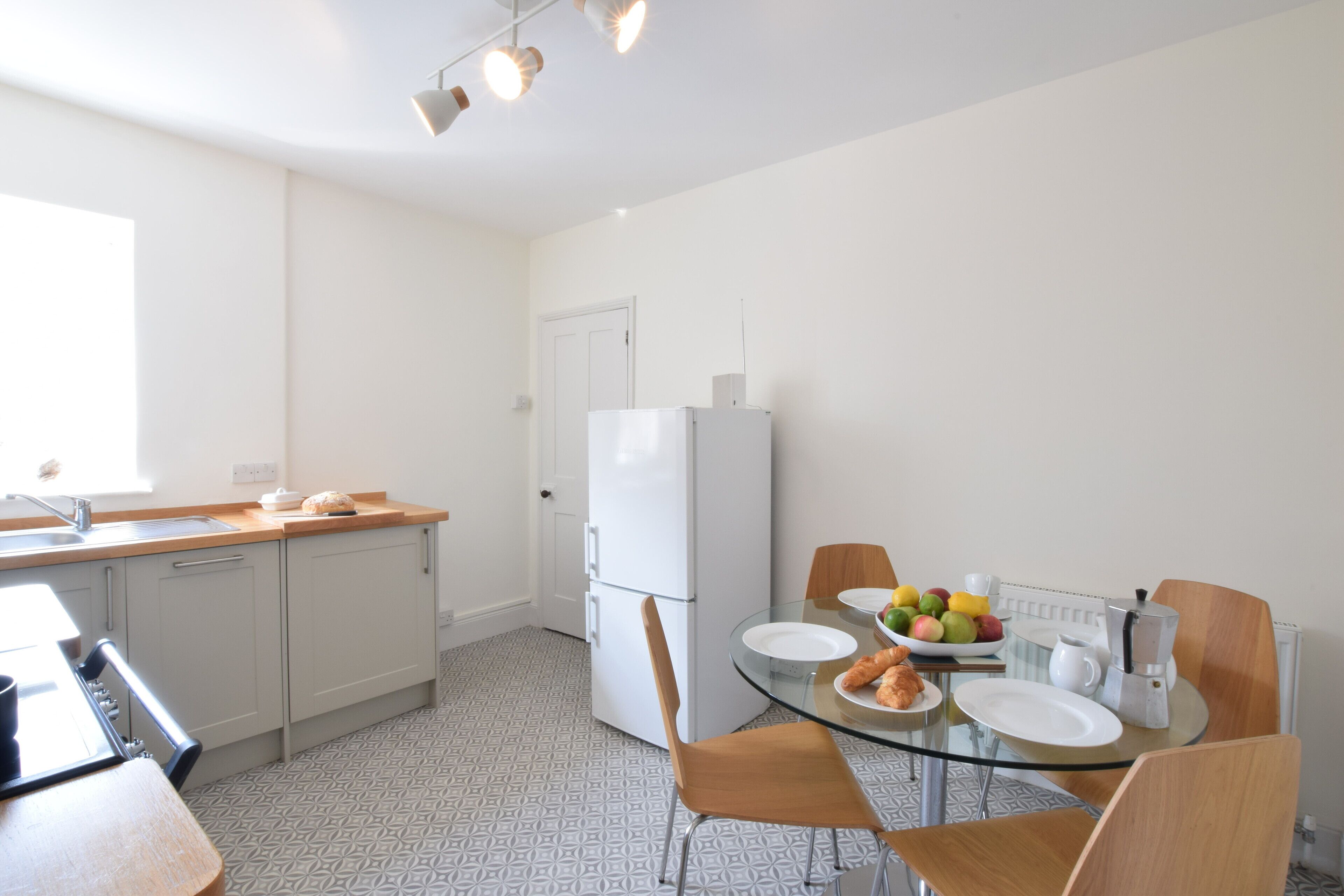 A modern kitchen with a dining table, chairs, a refrigerator, and a window providing natural light.