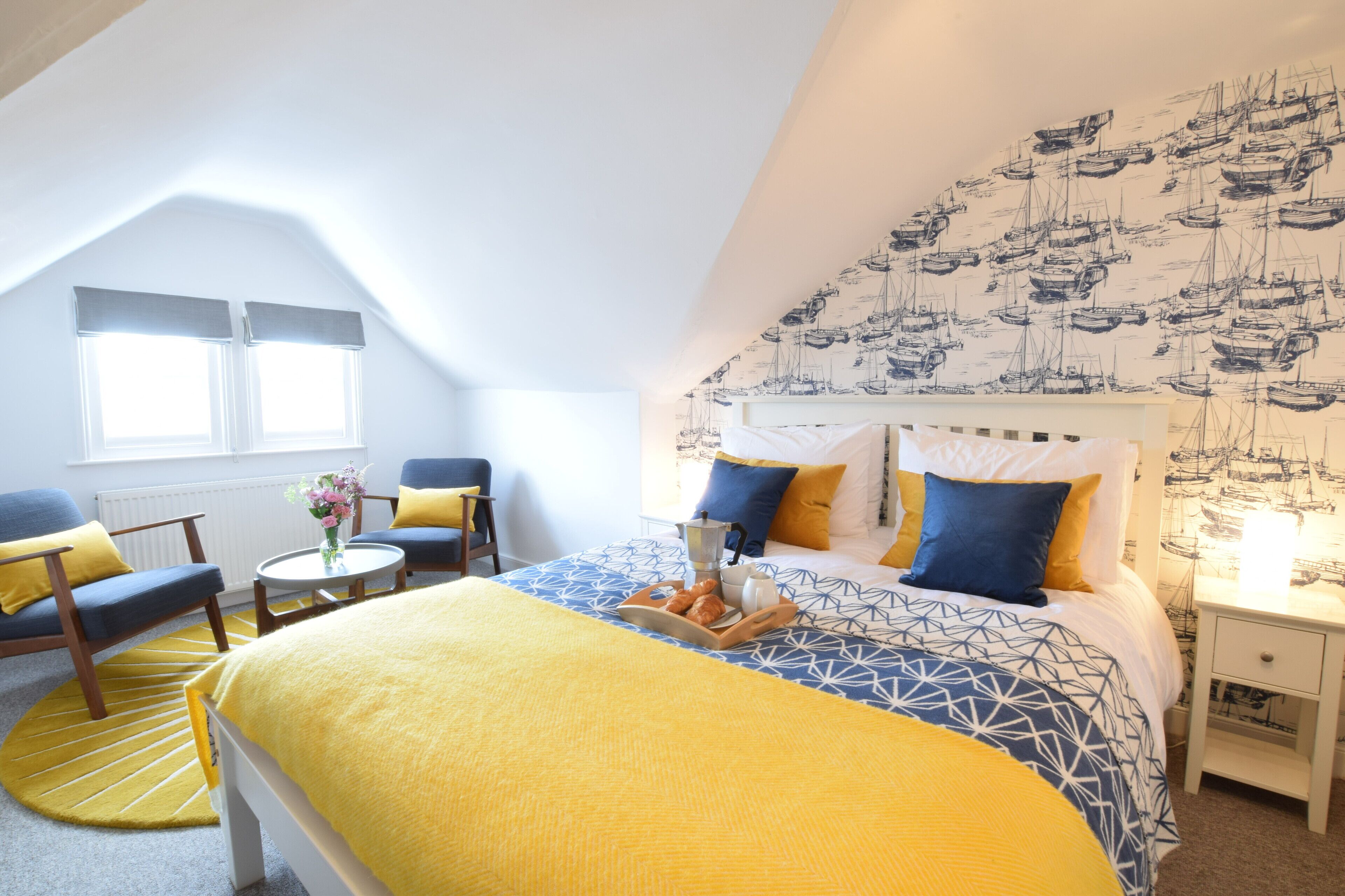 A bedroom with a bed, a nightstand, a chair, a table with a vase, and a window.