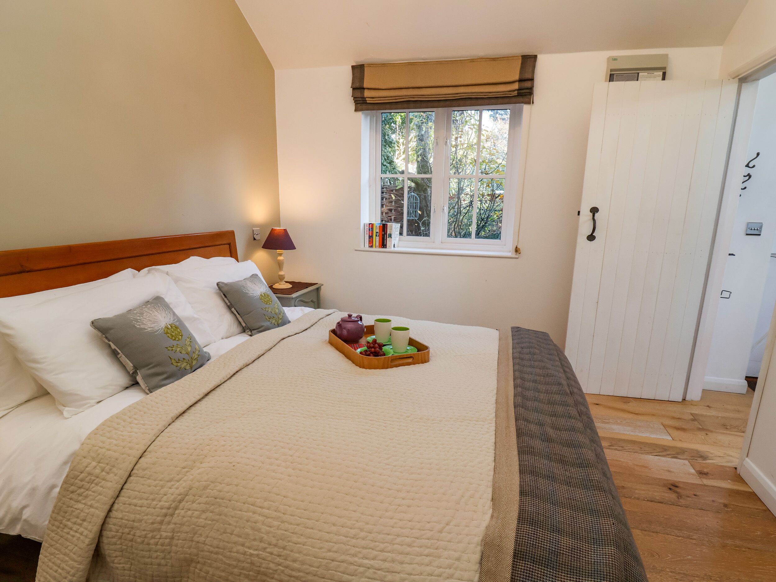 A bedroom with a bed, bedside table, lamp, window, and a door.