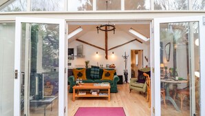 A spacious living room with a wooden floor, a green sofa, a wooden coffee table, and a red rug. - The Bothy at Snape Hall (Saxmundham)