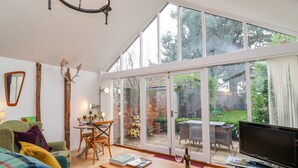 A spacious living room with a large TV, a dining area with a table and chairs, and a cozy seating area with a sofa and cushions. - The Bothy at Snape Hall (Saxmundham)