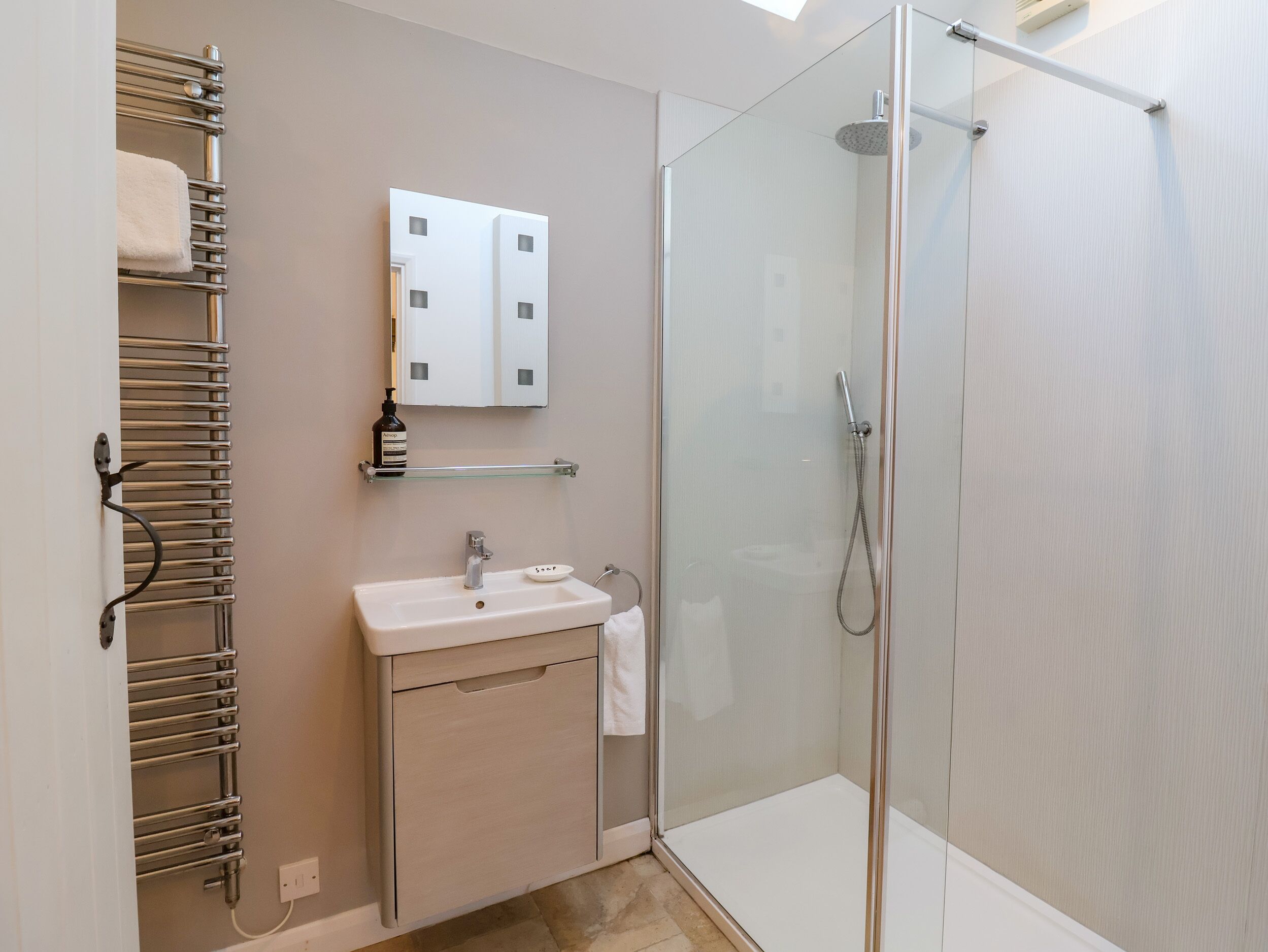 A modern bathroom with a glass-enclosed shower, a sink with a soap dish, and a towel rack.