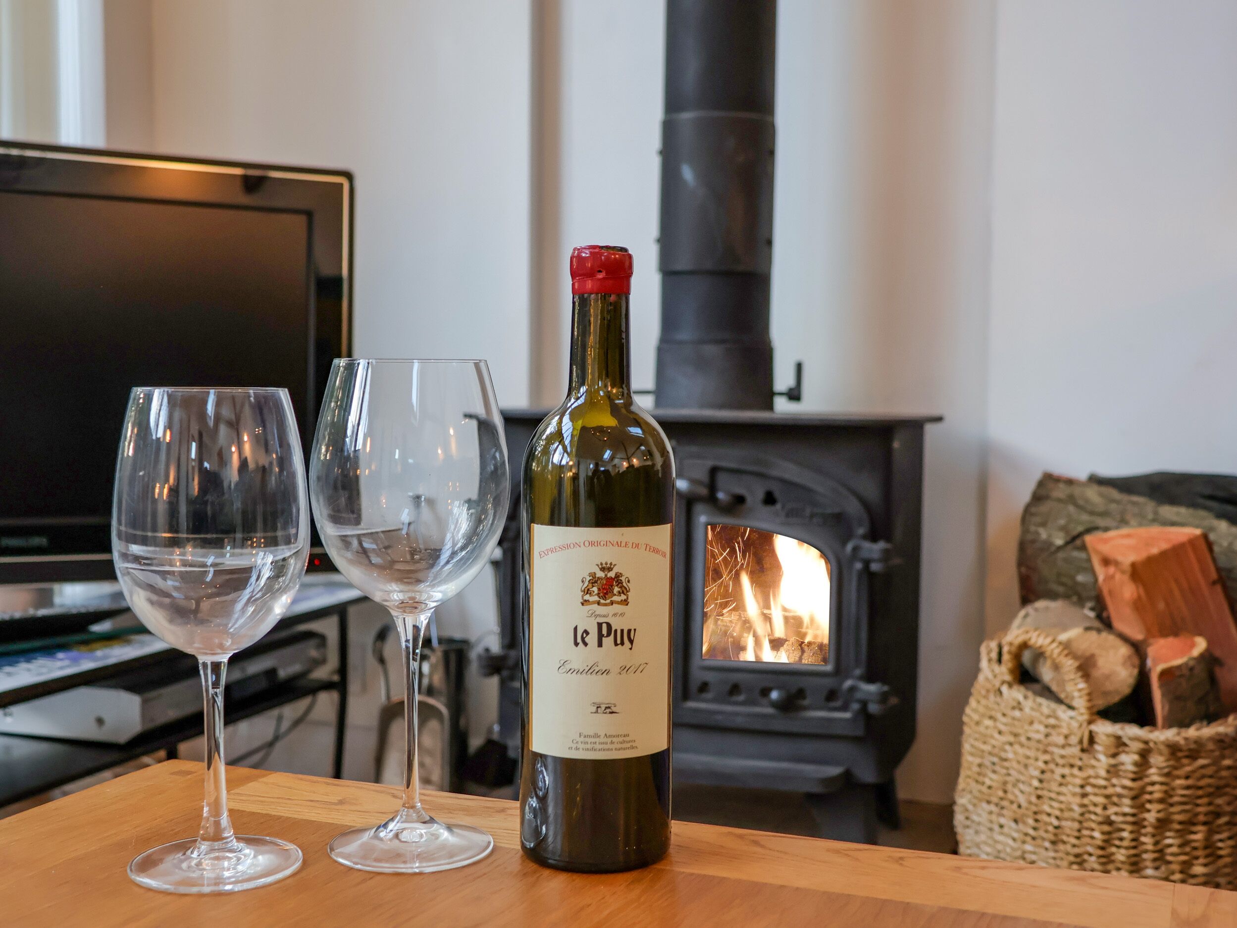 Una botella de vino y dos copas sobre una mesa de madera en una habitación con chimenea.