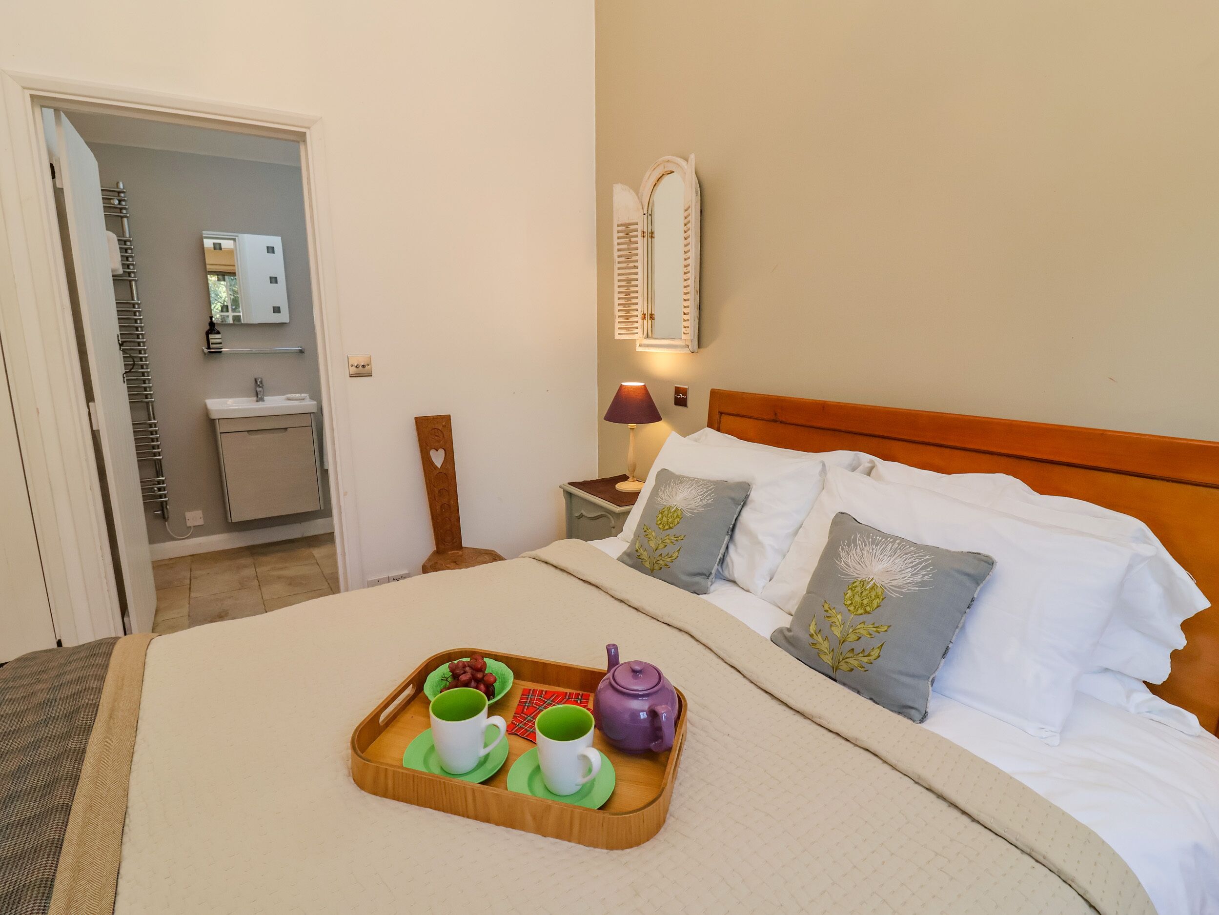 A neatly made bed with pillows, a bedside table with a lamp, and a tray with cups and a teapot on the bed.