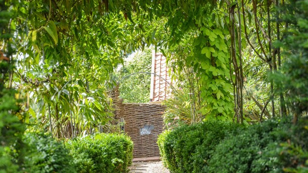 A stone pathway leading through a lush garden with a wicker archway and a sign reading "The Bothy". - The Bothy at Snape Hall (Saxmundham)