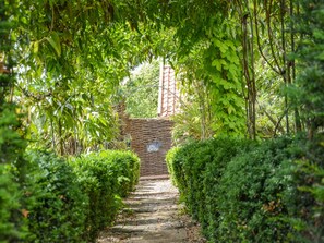 Een pad van stenen loopt door een weelderige tuin met een rieten bogenpoort en een bordje met de tekst 'The Bothy'.