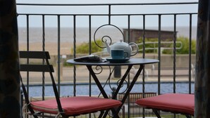 Uma varanda com mesa e cadeiras, um bule de chá e vista para o mar.