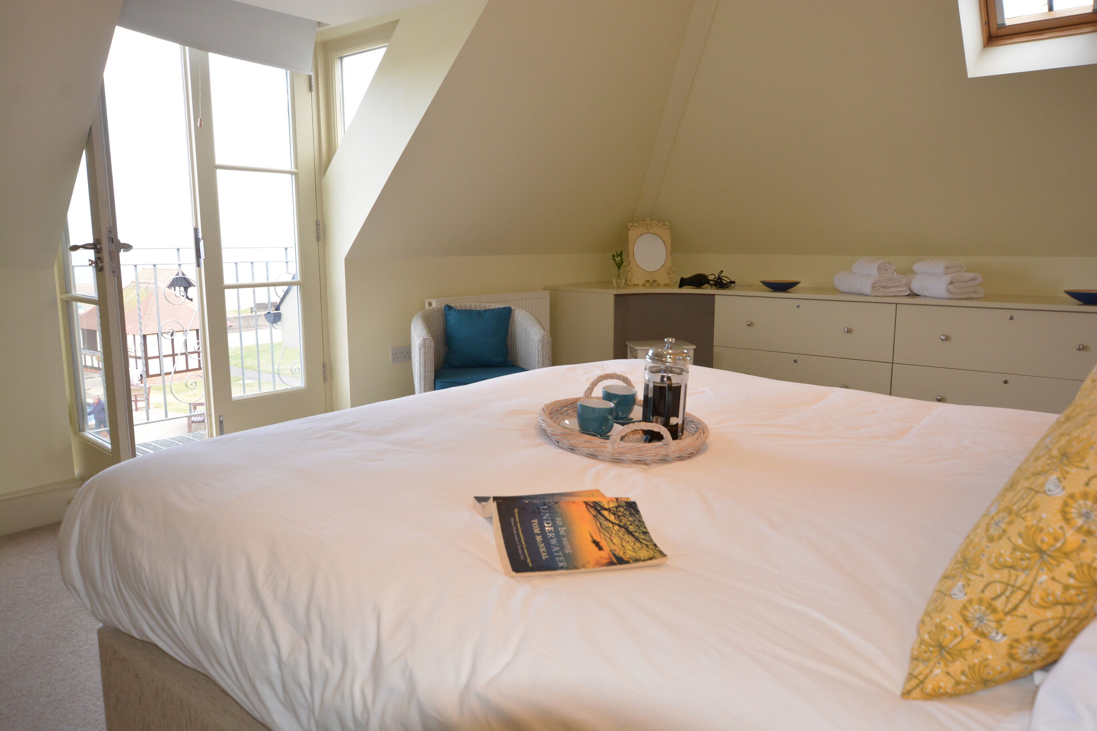 Une chambre à coucher avec un grand lit, une table de chevet sur laquelle se trouve un plateau de boissons, et une fenêtre donnant sur l’extérieur.