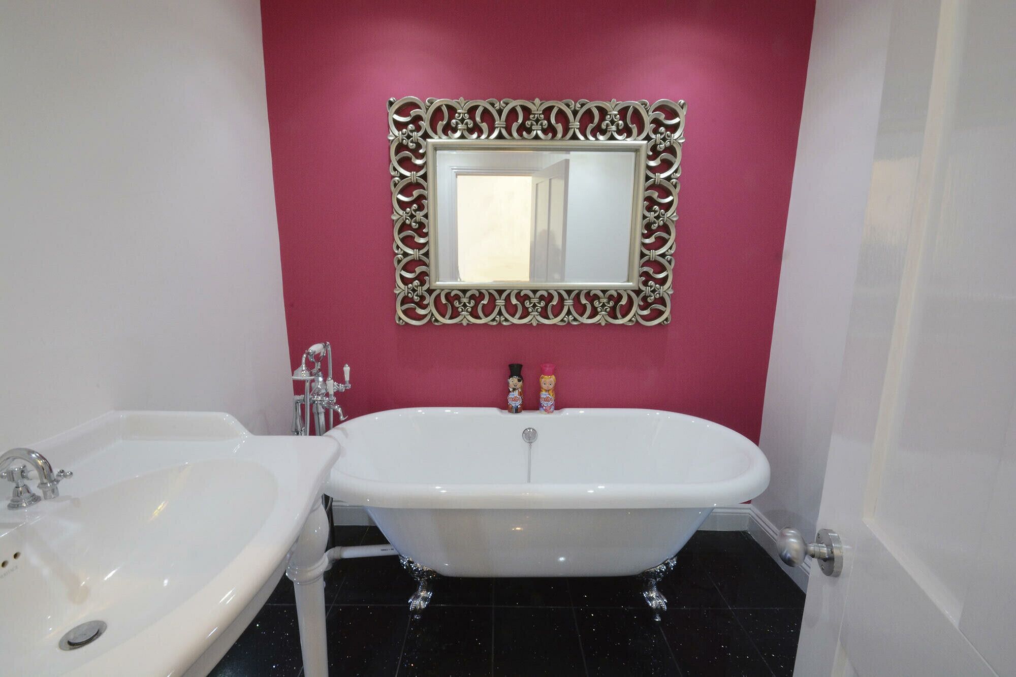 Un baño con una bañera blanca independiente, un lavabo blanco y un espejo decorativo con un marco ornamentado.