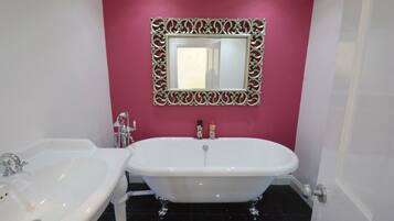 Un baño con una bañera blanca independiente, un lavabo blanco y un espejo decorativo con un marco ornamentado.