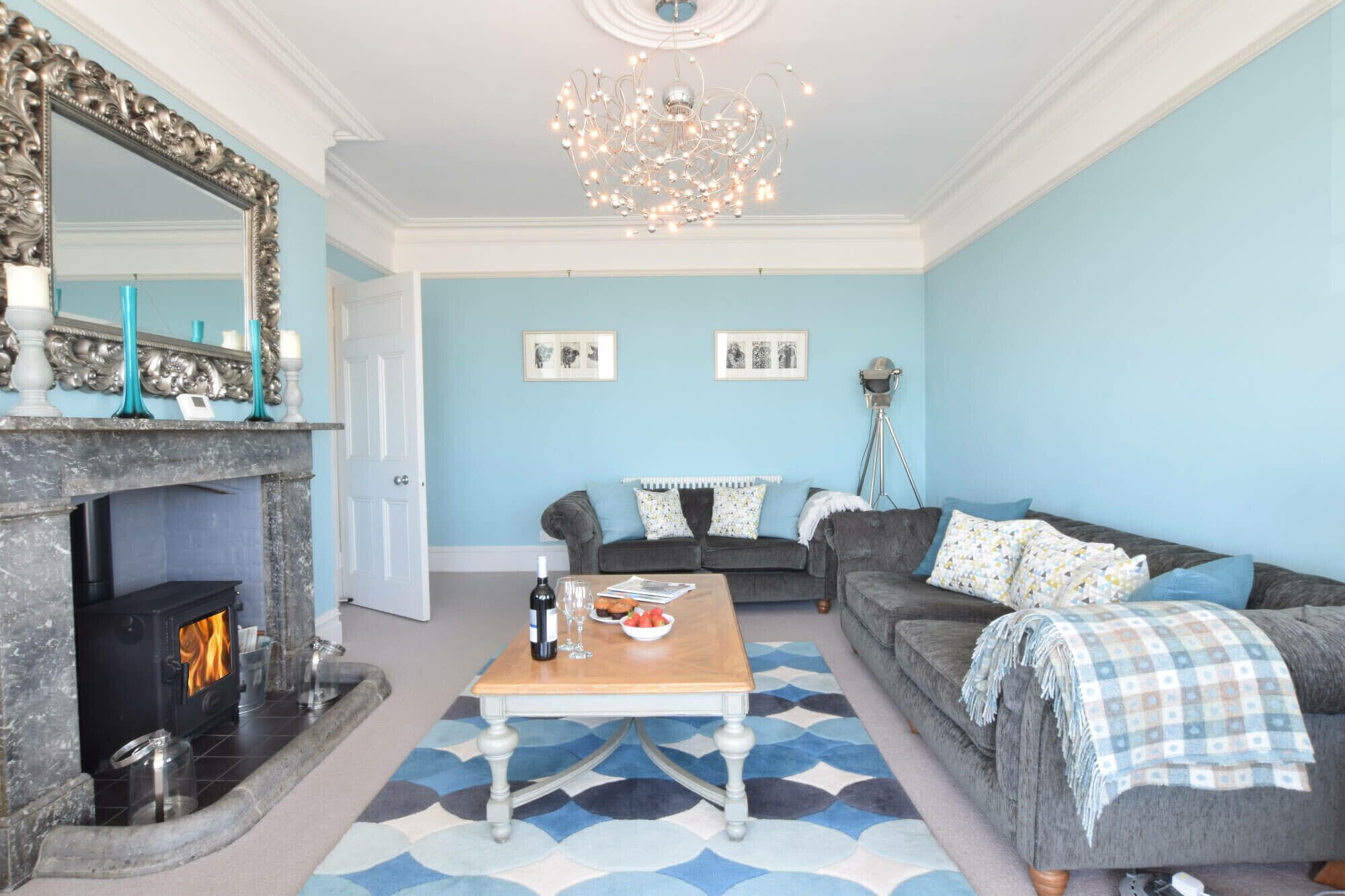 Een woonkamer met een open haard, een zithoek, een salontafel en een kroonluchter.
