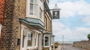 En traditionell pub med en skylt som visar texten ”ADNAMS THE LORD NELSON” och utsikt över havet i bakgrunden.