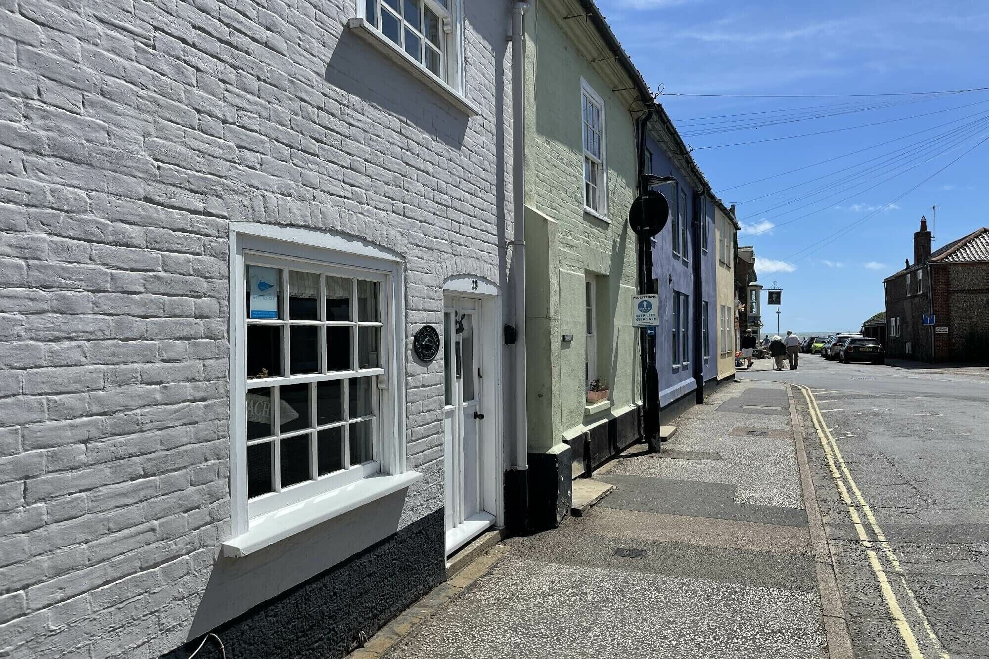 A white brick building with a row of windows and a door, a sign indicating a pedestrian zone, and a clear sky.