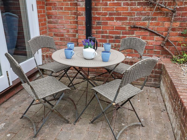 A round table with four wicker chairs, a white pot with purple flowers, and two blue cups on the table. - Dolphin Cottage, Southwold (Reydon)