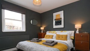 Ein Schlafzimmer mit einem Bett, zwei Nachttischen, einem Fenster, einem Spiegel und einer Wandlampe.