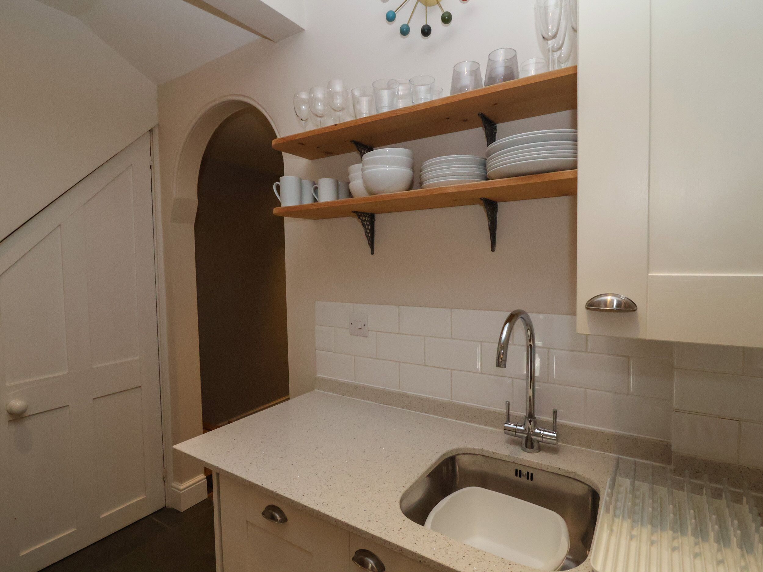 A kitchen with a sink, countertop, and shelves with dishes.