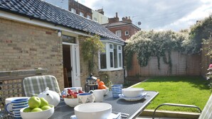 A patio area with a table set for a meal, surrounded by chairs and a brick wall. - Garden Cottage, Southwold (Reydon)