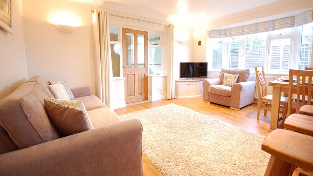 A cozy living room with a sofa, a TV, and a dining area with chairs and a table. - Garden Cottage, Southwold (Reydon)