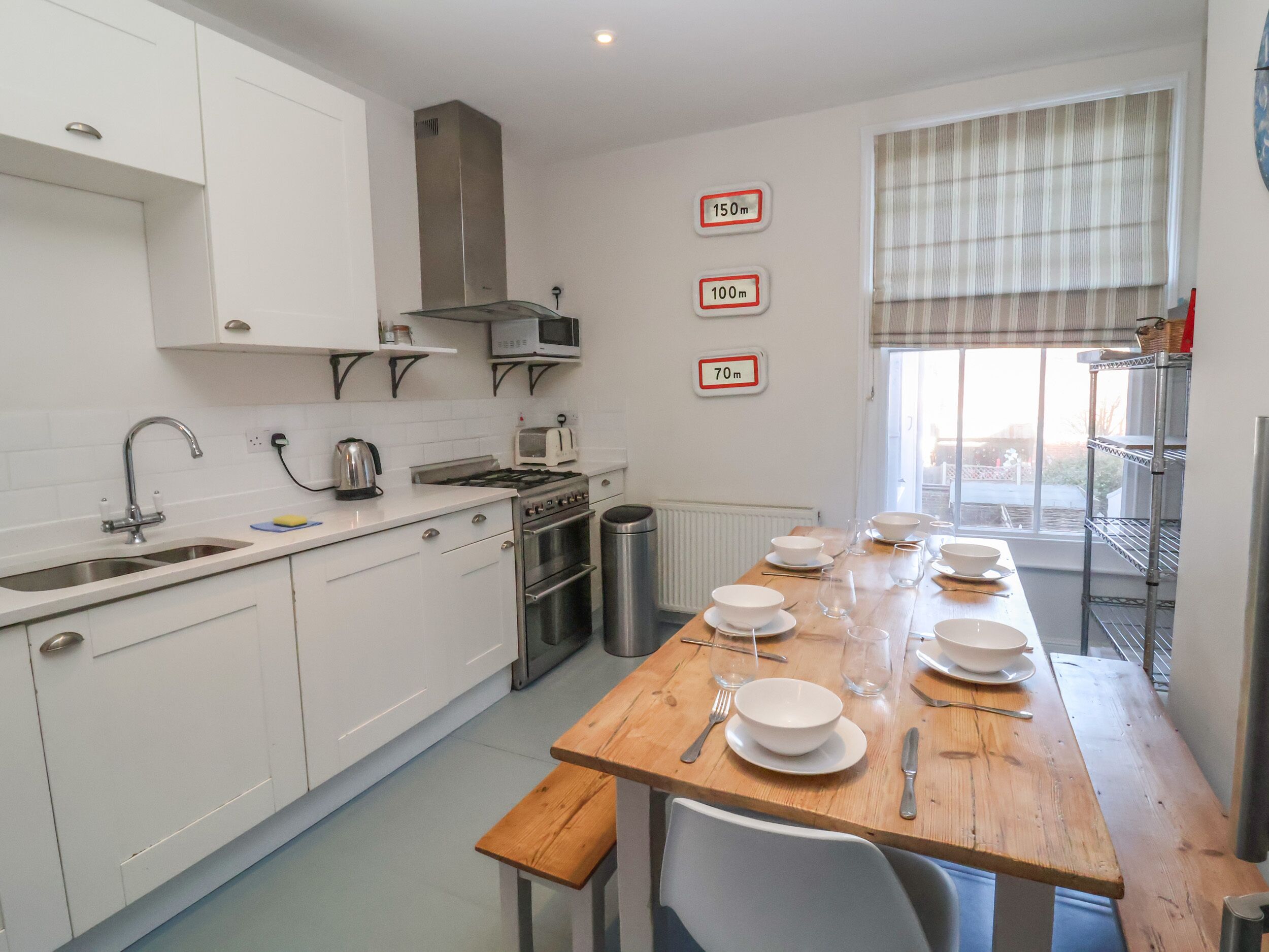 Une cuisine moderne avec des meubles blancs, un évier en acier inoxydable, un four à micro-ondes, une cuisinière et une table à manger agrémentée de bols et de verres.