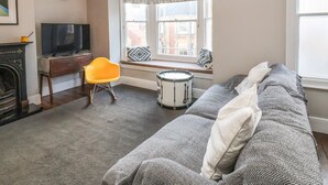 Ein Wohnzimmer mit einer Couch, einem Fernseher, einem Kamin, einer Trommel und einem Fenster mit Vorhängen.