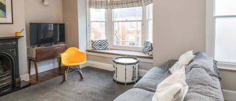 A living room with a sofa, a television, a fireplace, a drum, and a window with curtains.