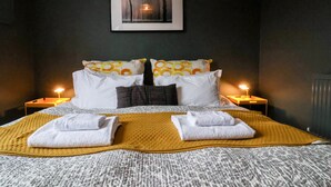 Ein ordentlich bezogenes Bett mit einem gemusterten Überwurf, zwei Kissen mit einem kreisförmigen Design und zwei gefaltete Handtücher auf dem Bett.