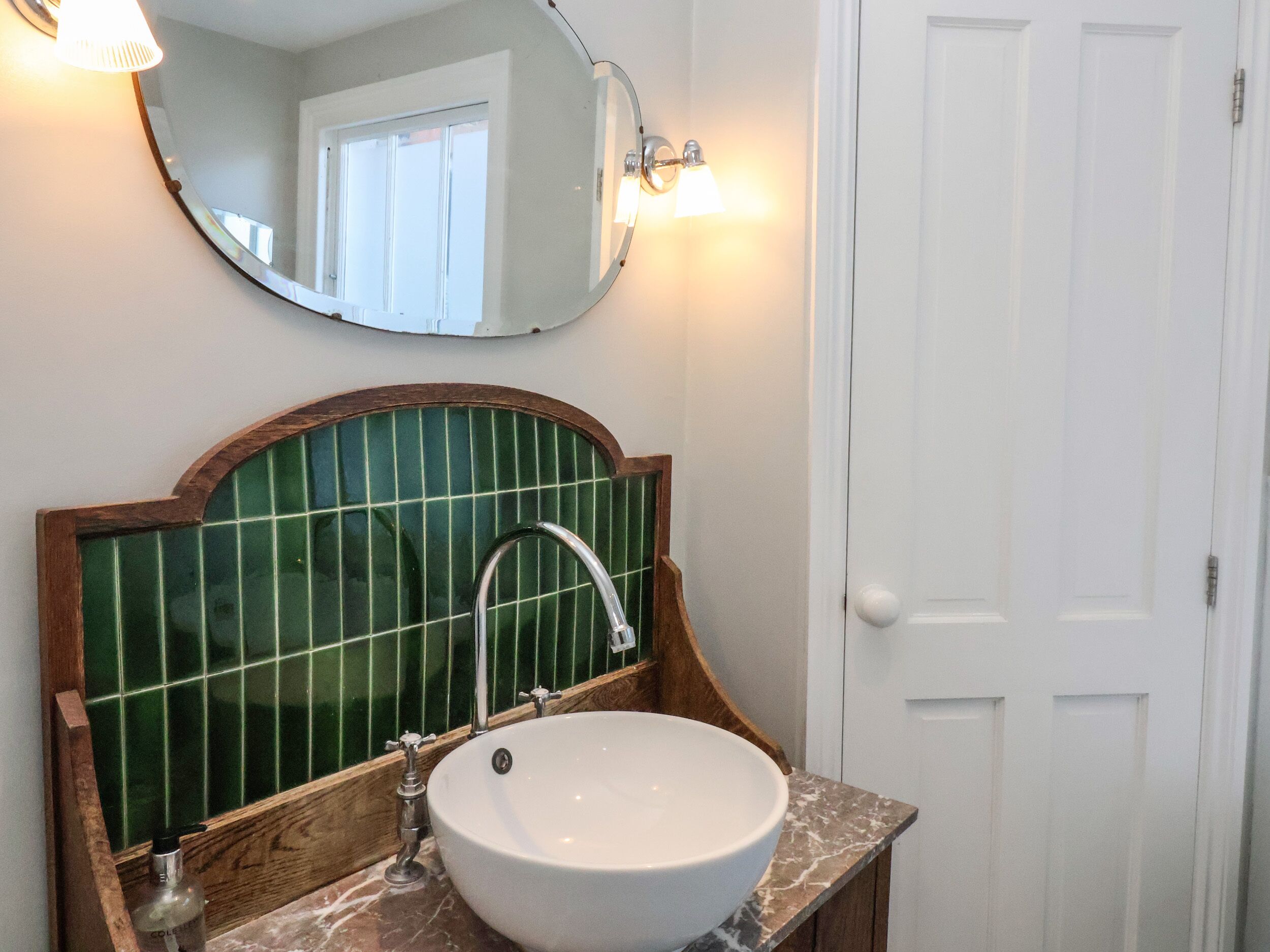 Een badkamer met een witte wasbak, een groen betegelde spatwand en een spiegel met houten lijst.