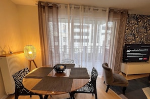 A dining area with a table, chairs, a lamp, and a television. - Appartement 6 personnes, 5mn Disneyland Paris, Val d'Europe + Captain America ++ (Chessy)