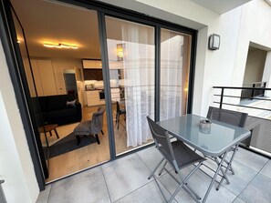 A modern apartment with a glass door leading to a living area, a balcony with a table and chairs, and a kitchen visible through the glass. - Appartement 6 personnes, 5mn Disneyland Paris, Val d'Europe + Captain America ++ (Chessy)