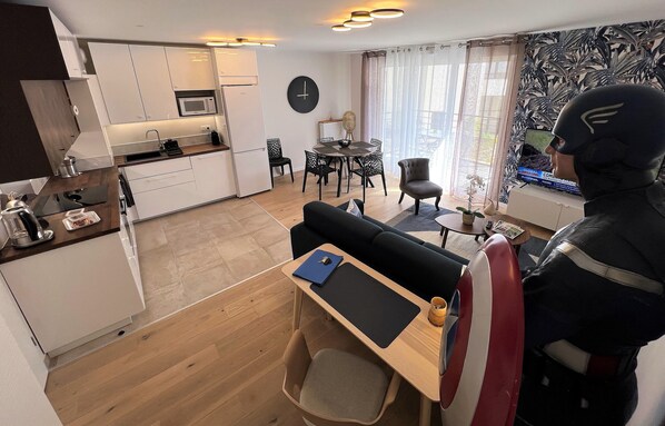 A compact living space with a kitchenette, dining area, and a seating area with a view. - Appartement 6 personnes, 5mn Disneyland Paris, Val d'Europe + Captain America ++ (Chessy)