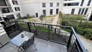 A balcony with a glass table and chairs, overlooking a courtyard with plants and a pathway. - Appartement 6 personnes, 5mn Disneyland Paris, Val d'Europe + Captain America ++ (Chessy)