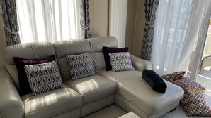 Un canapé en cuir beige agrémenté de coussins à motifs, une table basse en bois clair et des rideaux transparents qui laissent passer la lumière naturelle.