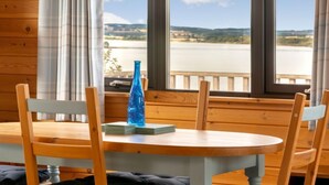 A wooden cabin room with a round table and chairs, a blue vase, and a view of a lake and hills. - Lodge 9 by Interhome (Kinross)