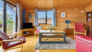 A cozy cabin interior with wooden walls and floors, a dining table with chairs, a sofa, a TV, and a bookshelf. - Lodge 9 by Interhome (Kinross)