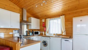 A compact kitchen with wooden walls, a washing machine, a microwave, a sink, and a refrigerator. - Lodge 9 by Interhome (Kinross)