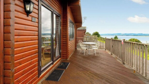 A wooden deck with a table and chairs, a view of the water, and a wooden fence. - Lodge 9 by Interhome (Kinross)
