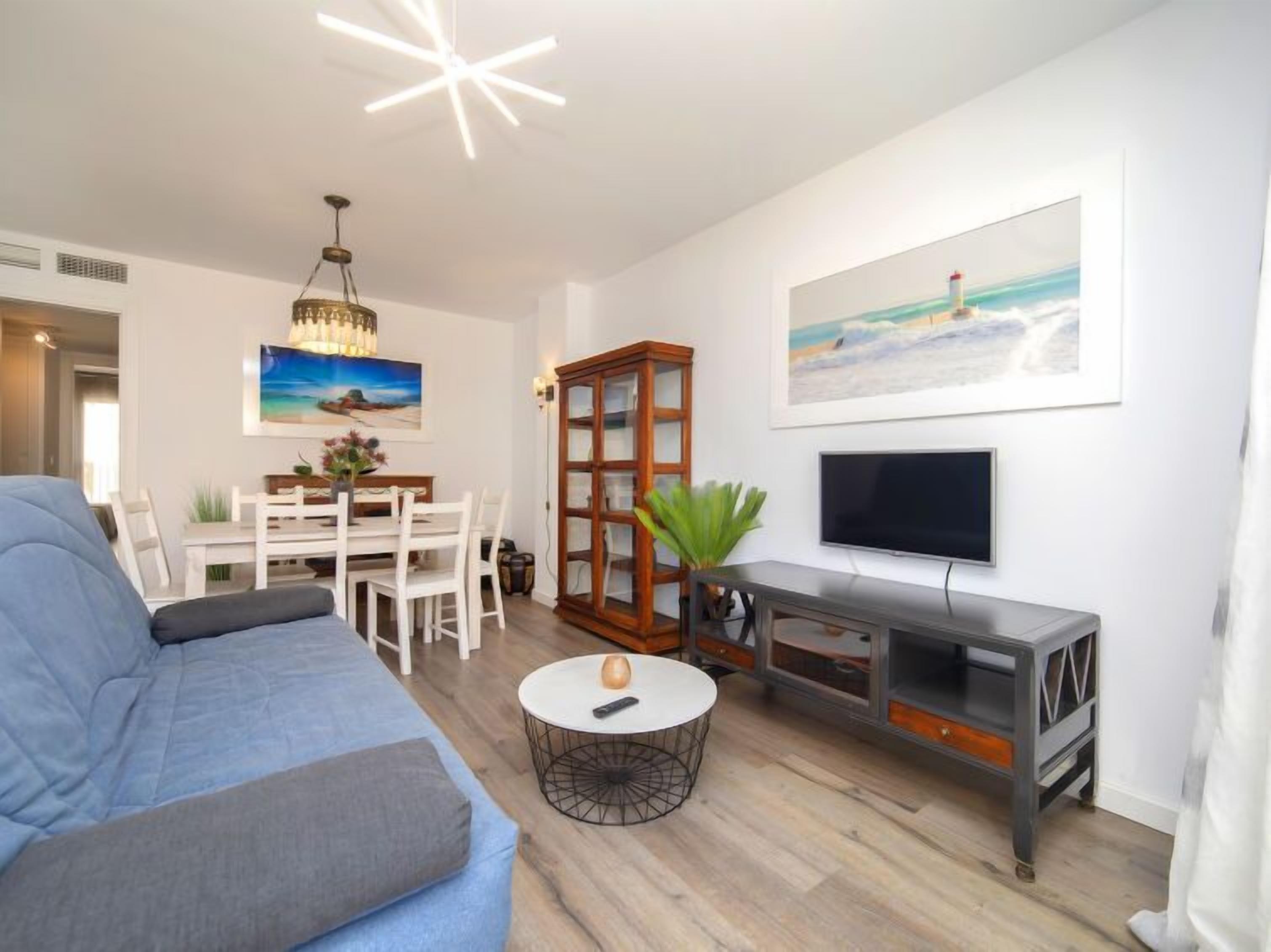 A living room with a blue sofa, a dining table with chairs, a TV, and a bookshelf.